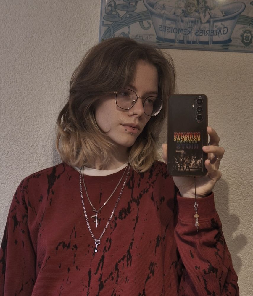 mirror selfie of me wearing a red shirt with black marble-like patterns. I am looking at my phone.