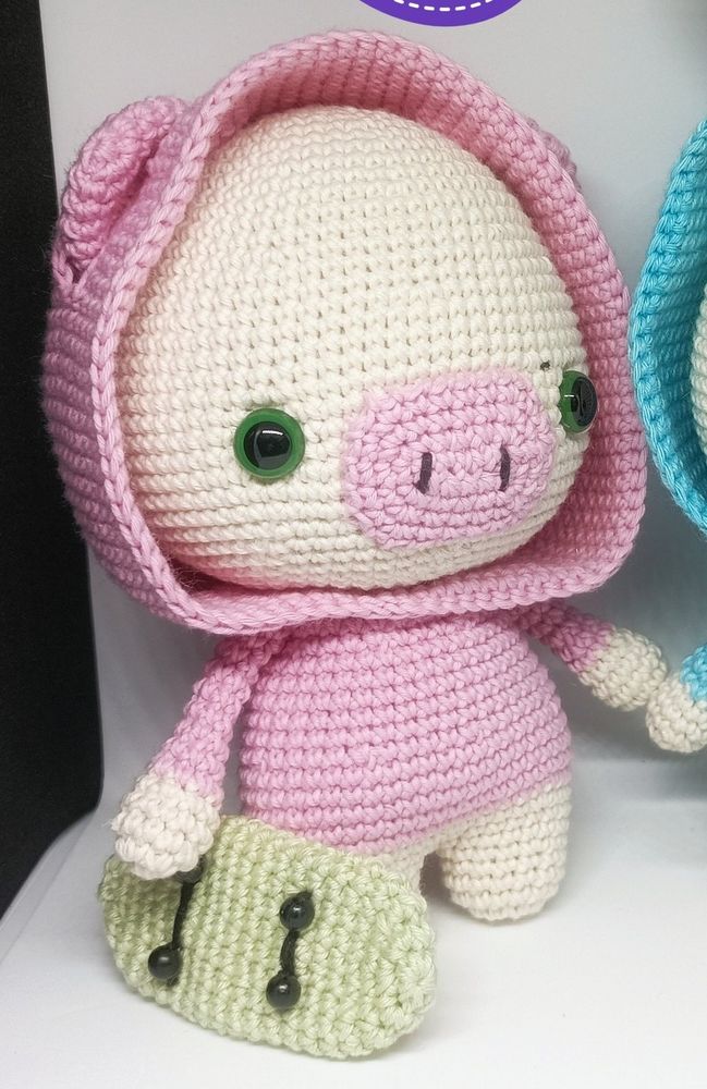 a crocheted doll of a piggy in pink hoodie, green eyes, and small green skateboard