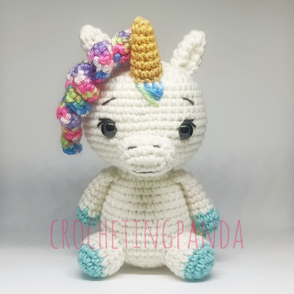 Amigurumi doll of a small unicorn with white body, light blue hooves, and multicolored hair