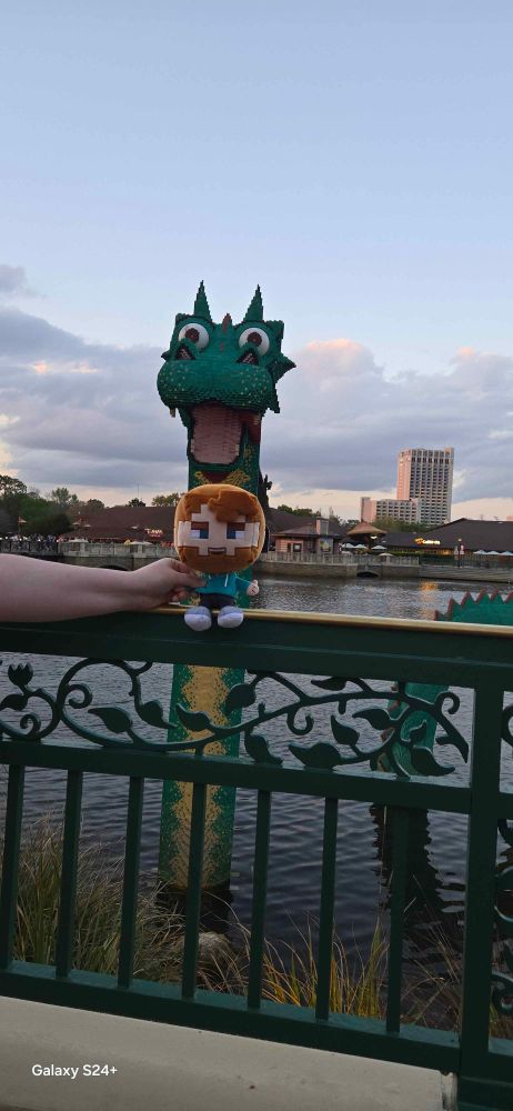 A green sea monster, made of Lego bricks, in a lagoon. A stuffed Fwhip character is in the foreground.