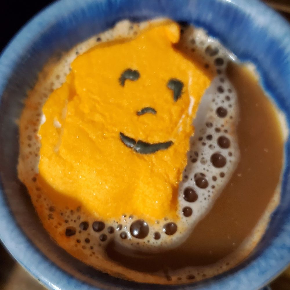An orange Halloween Pumpkin Peep with a smiling face floating in a cup of coffee.
