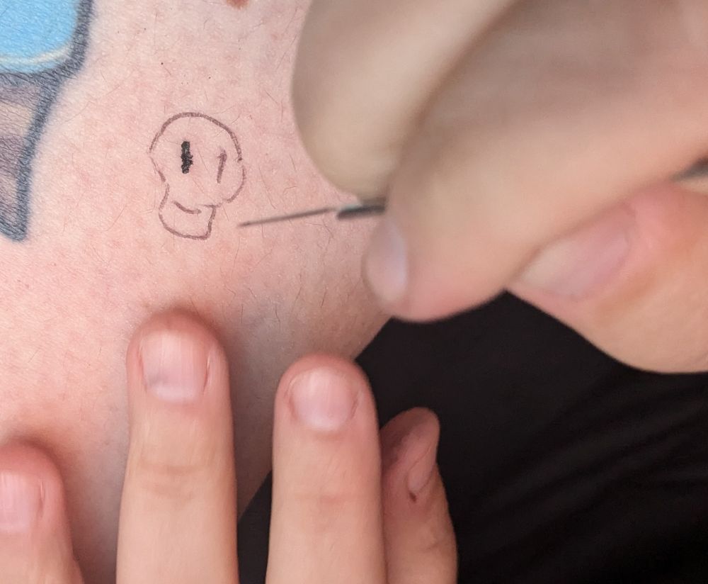 Tiny skull being tattooed on a knee, stick-and-poke style