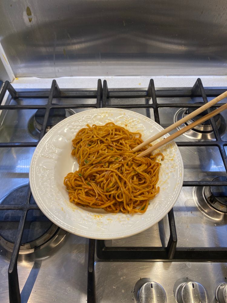 A bowl of gochujang spicy noodles in a white bowl accompanied by chopsticks 