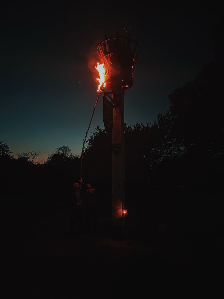 Two people using a large stick to light a beacon with fire