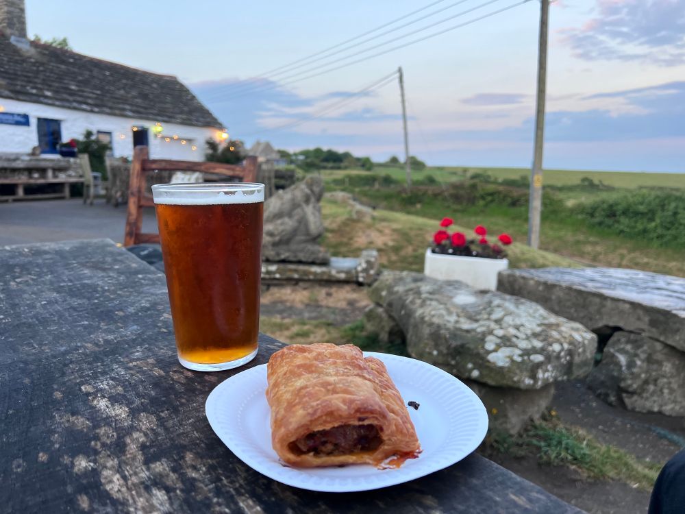 Pint and sausage roll in front of some stone benches at a Dorset pub