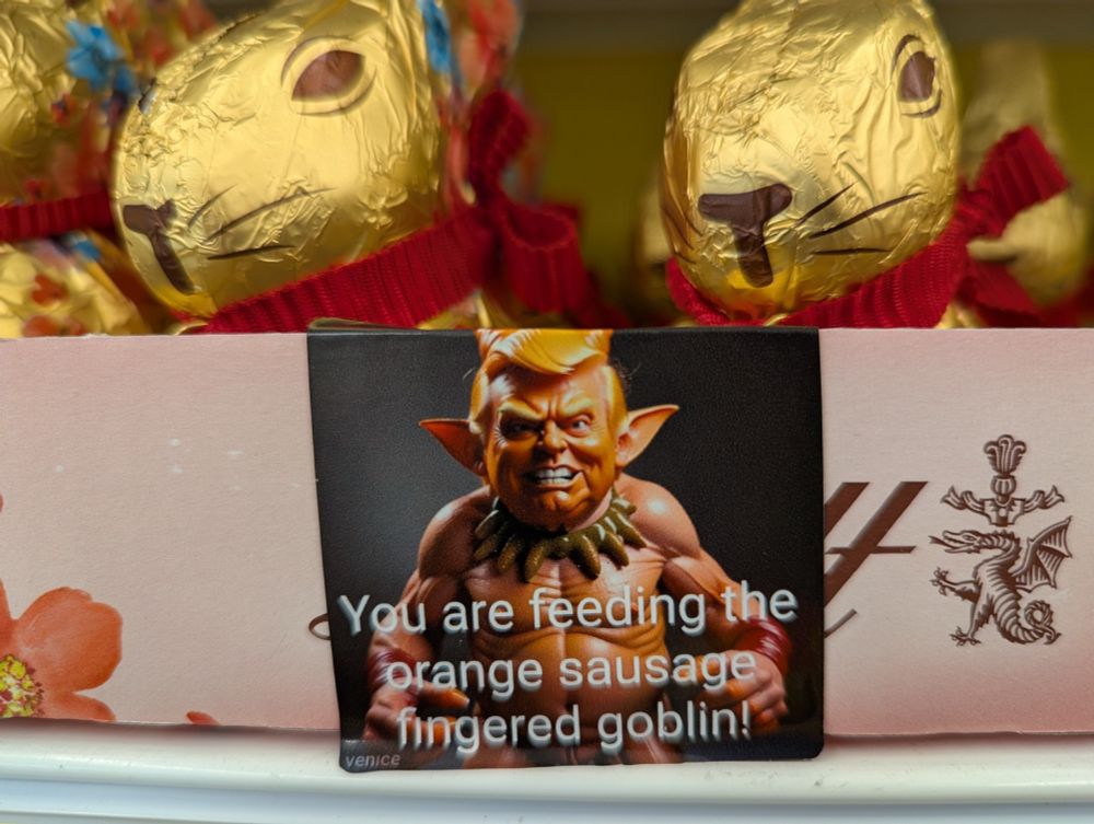 A store display of Lindt chocolate bunnies with a sticker added that says "You are feeding the orange sausage fingered goblin!"  The sticker has an image of a goblin-like creature that looks like Donald Trump.