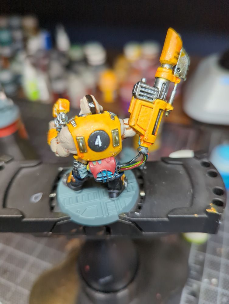 The back of an Ogryn model on a painting handle. The carapace armor is painted yellow and is numbered '4'.