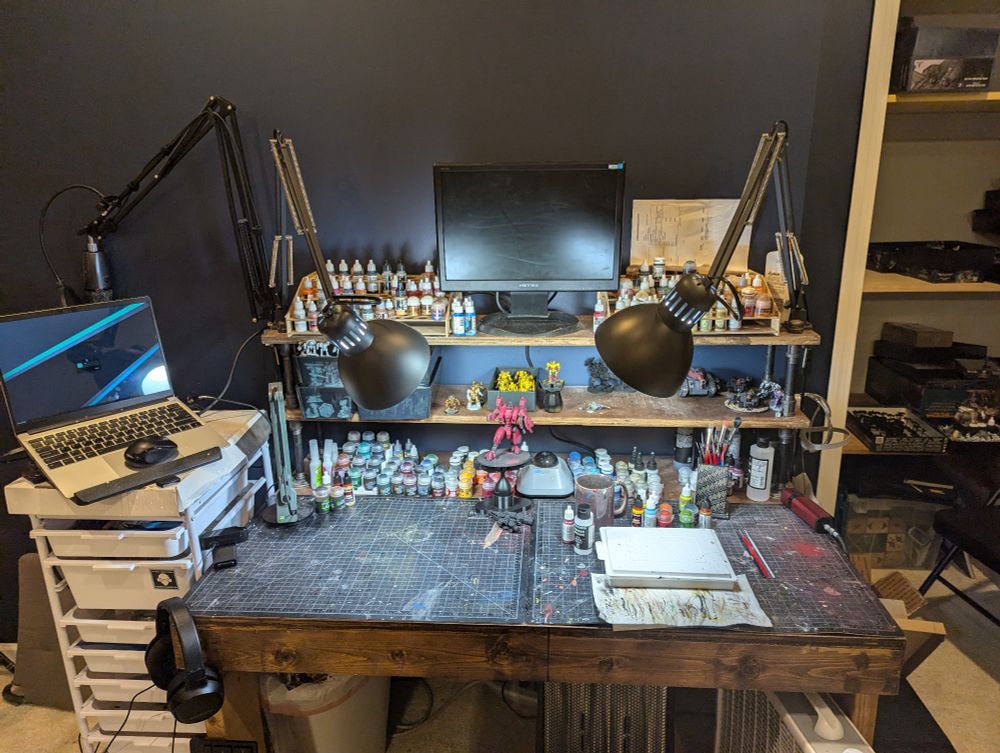 A hobby desk with two shelves, several paint racks for storing model paints, and two large self healing cutting mats for the work surface