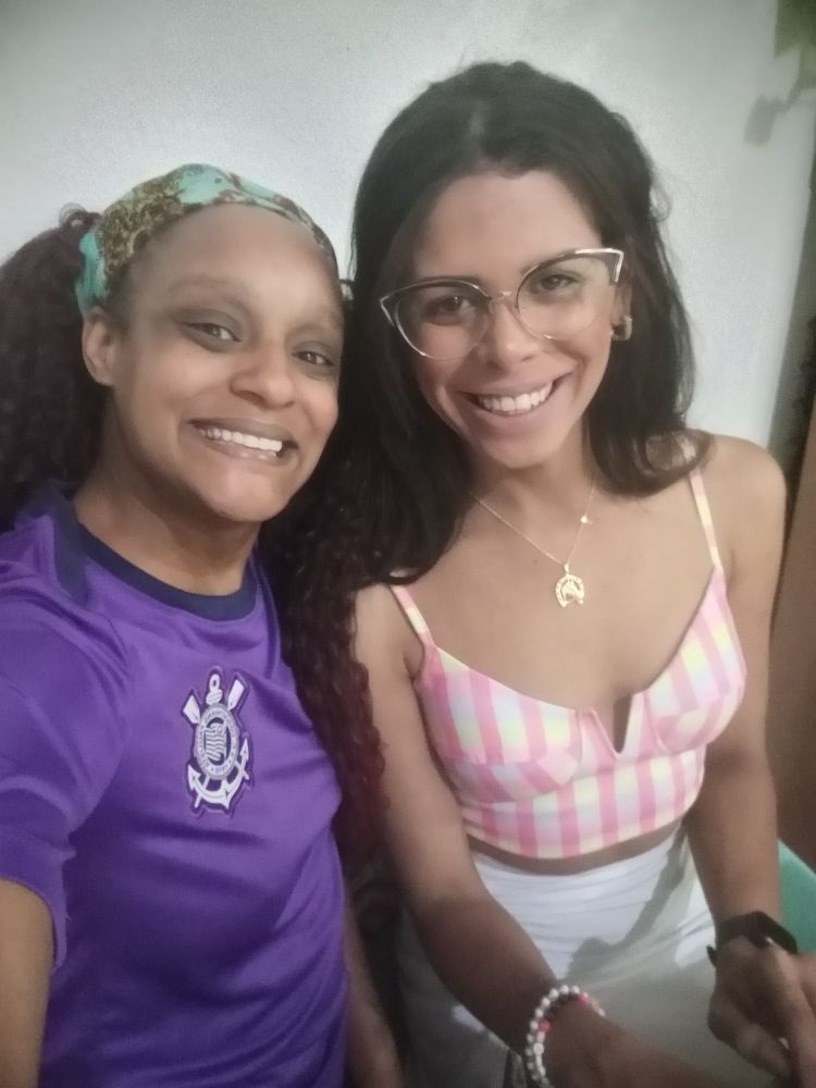 Mulher preta camiseta do Corinthians roxa e lenço na cabela azul e mulher parda cabelo castanho longo cropped quadriculado ensaia branca e usa óculos de gatinha 