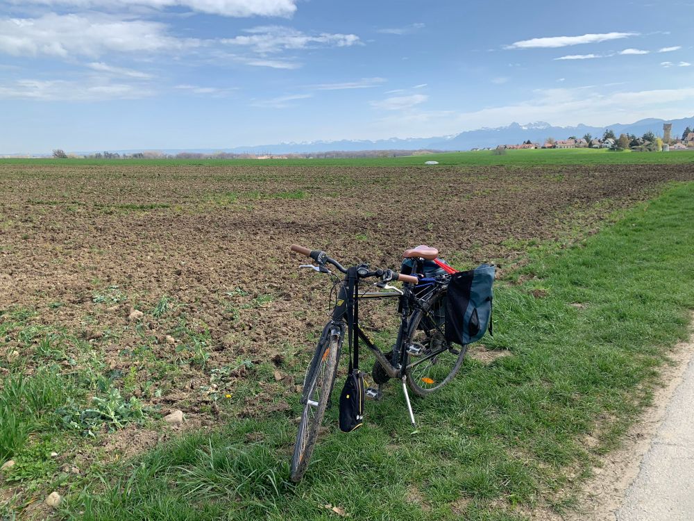 Bike in a field with the alps in the background. On the bike is a bag with a gps and some markers