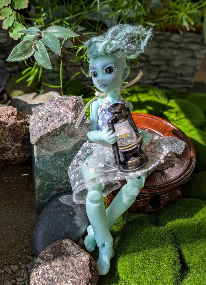 Ethyl, the @teenytinker.bsky.social Nyx ball jointed doll, sits on a wooden pedestal in the indoor garden, holding an unlit lantern.