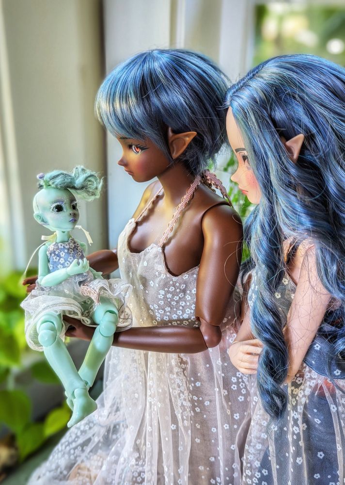Ethyl, a Nyx bjd from @teenytinkers is held by Beatrix, a Smart Doll Pear in cocoa, while Twyla, a Smart Doll in cinnamon, looks over Beatrix's shoulder.