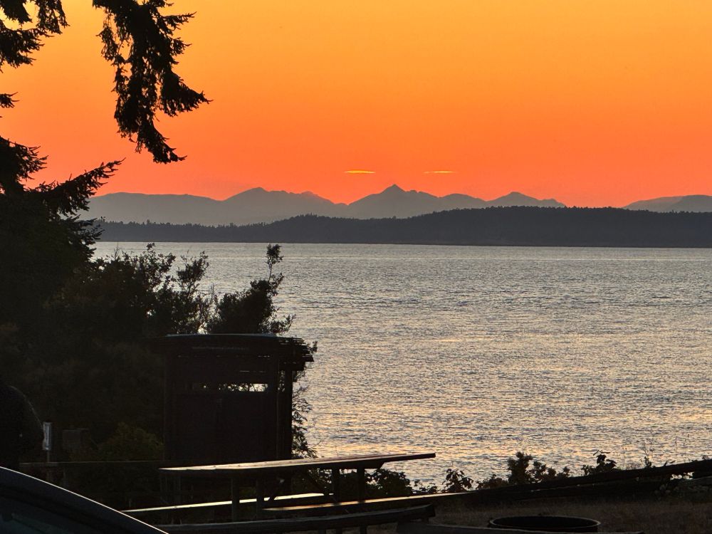 A picnic table, the sea and mountains with a sunset 