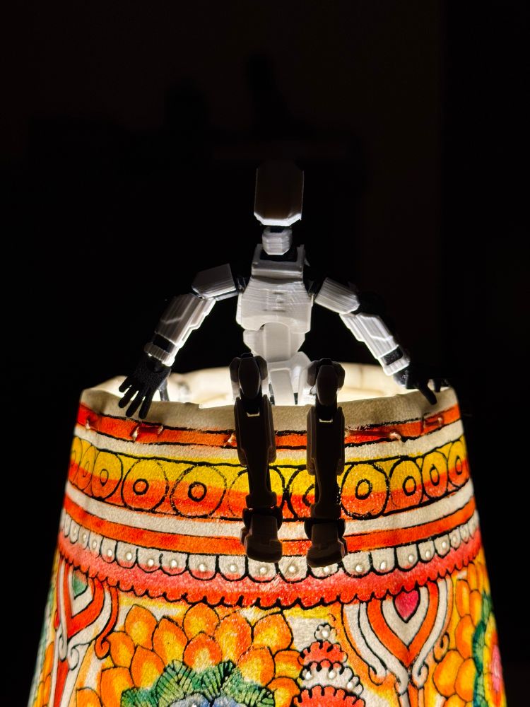 A 3D printed and assembled figurine in black and white placed on a table lamp.