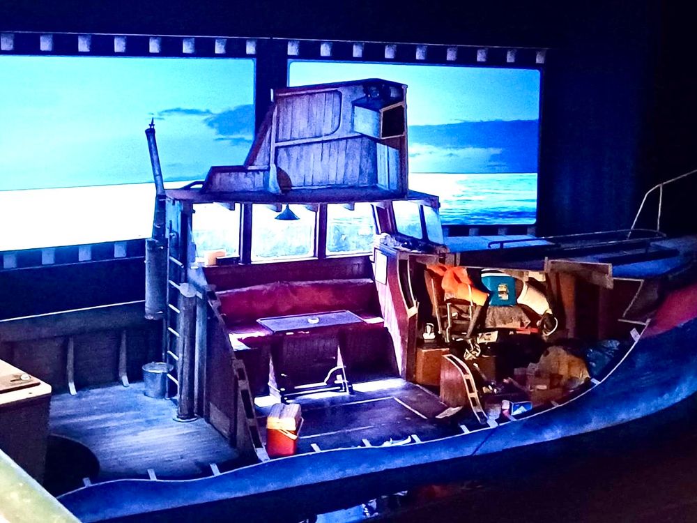 A theatre stage featuring a boat with the roof cut away showing the inside of the cabin.
