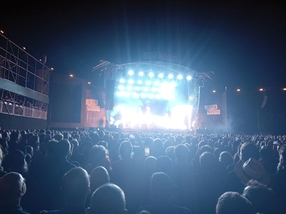 Scène principale du festival Lokerse Feesten avec la scène arrosée de lumière (flammes) devant des têtes de spectateurs 