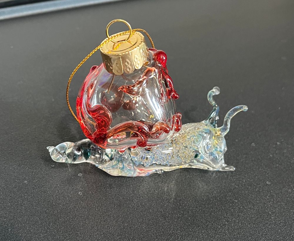 Other side view of a glass snail Christmas ornament with a speckled body and a red swirly shell. It is topped by a gold ornament cap and gold string. 