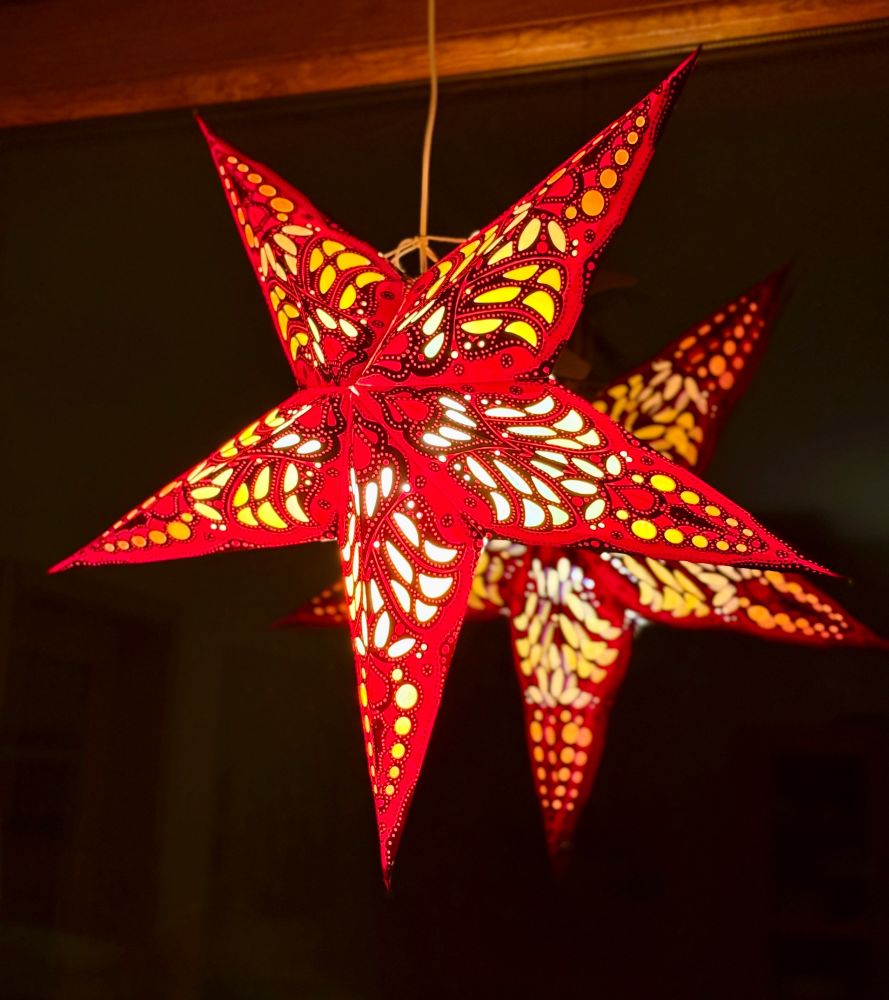 Ein roter beleuchteter Weihnachtsstern hängt von der Decke runter am Fenster. Im Fenster spiegelt sich der Stern. Der Hintergrund ist schwarz. 
