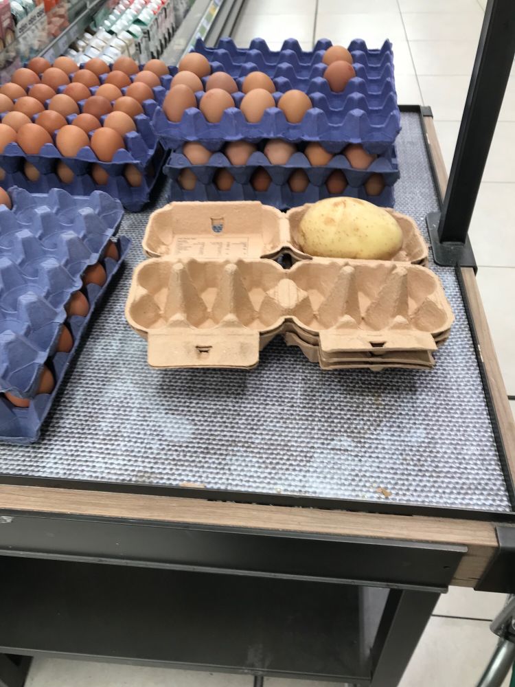 Picture is of egg trays and boxes, the trays are filed with normal hens eggs, one of the boxes holds a potato.