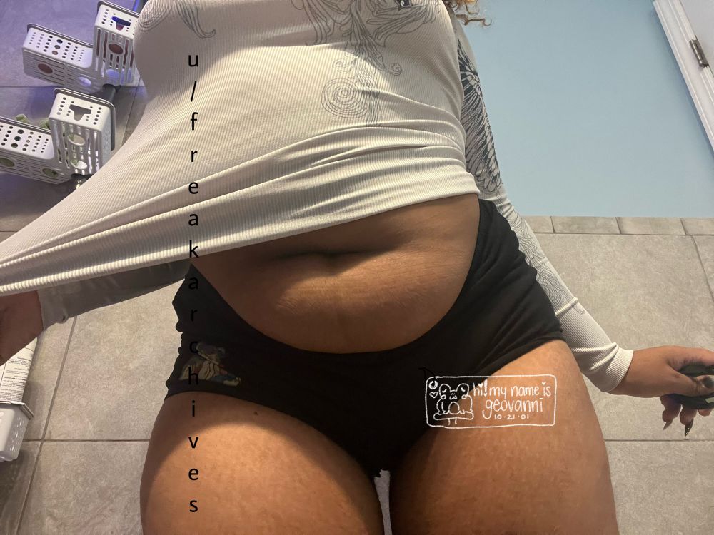 me from the front, standing with black shorts on & a white long sleeve shirt, pulling the shirt playfully off of my torso. 