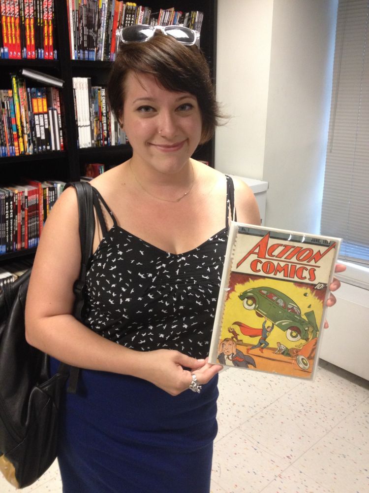 A younger one with short hair holds a copy of Action comics number one, which contains the first appearance of Superman. Superman lifts the green car above his head.