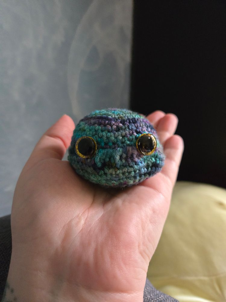 Mini crocheted dragon head in blues and purples with orange eyes