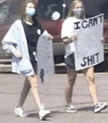 two girls presumably at a protest during covid times. the sign says "I CAN'T [unintelligible] SHIT"
