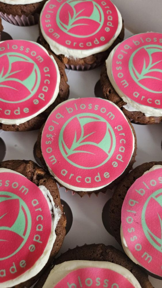 A picture with many chocolate cupcakes with the Blossom Arcade pink and green logo on the top of them, it is a circle logo with three leaves blooming together.