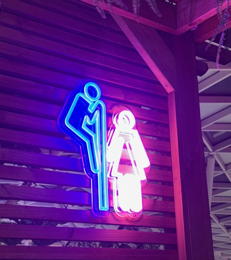 Pictogramme indiquant les toilettes d'un bar : le petit bonhomme bleu regarde au dessus du mur pour voir le petit bonhomme rose 