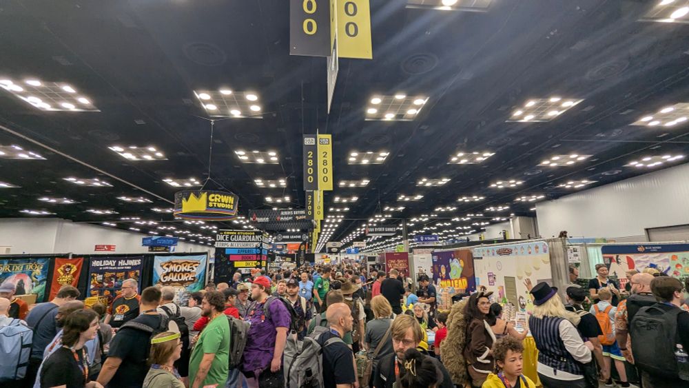 A photo of a crowd of people on the GenCon floor all looking at booths with different games or games accessories. 