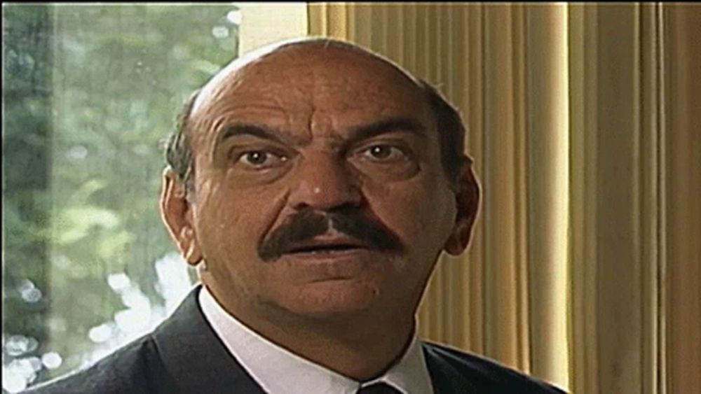 a bald man with a mustache is looking at the camera