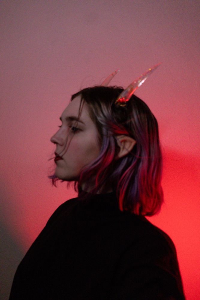 Woman with horns and pointed ears in front of a red background 