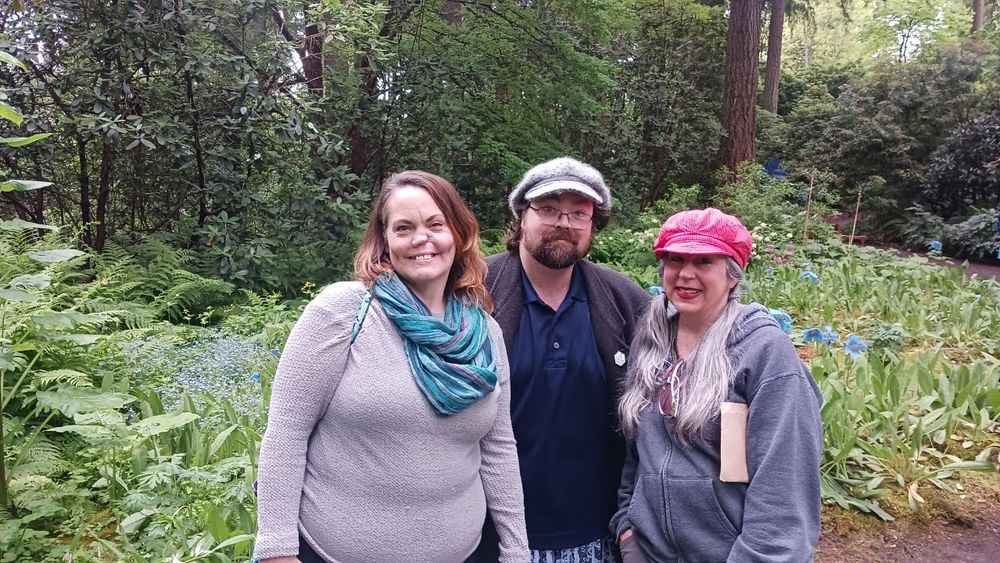 Three people standing in front of a field of blue poppies in a green forest