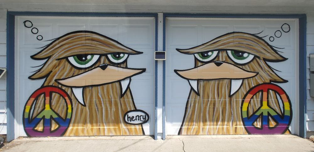 Paintings of Sasquatch with rainbow peace signs by artist Henry  on two garage doors
