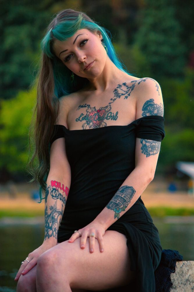 Vixey Vex in a black dress sitting in front of a lake with a forest in the background