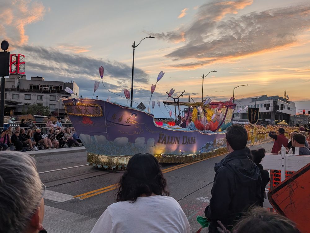 Falun Dafa float, shaped like a ship with lights and decorations, with the sunset in the background