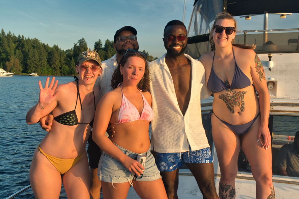A group of friends stands on the bow of a boat on Lake Washington at golden hour
