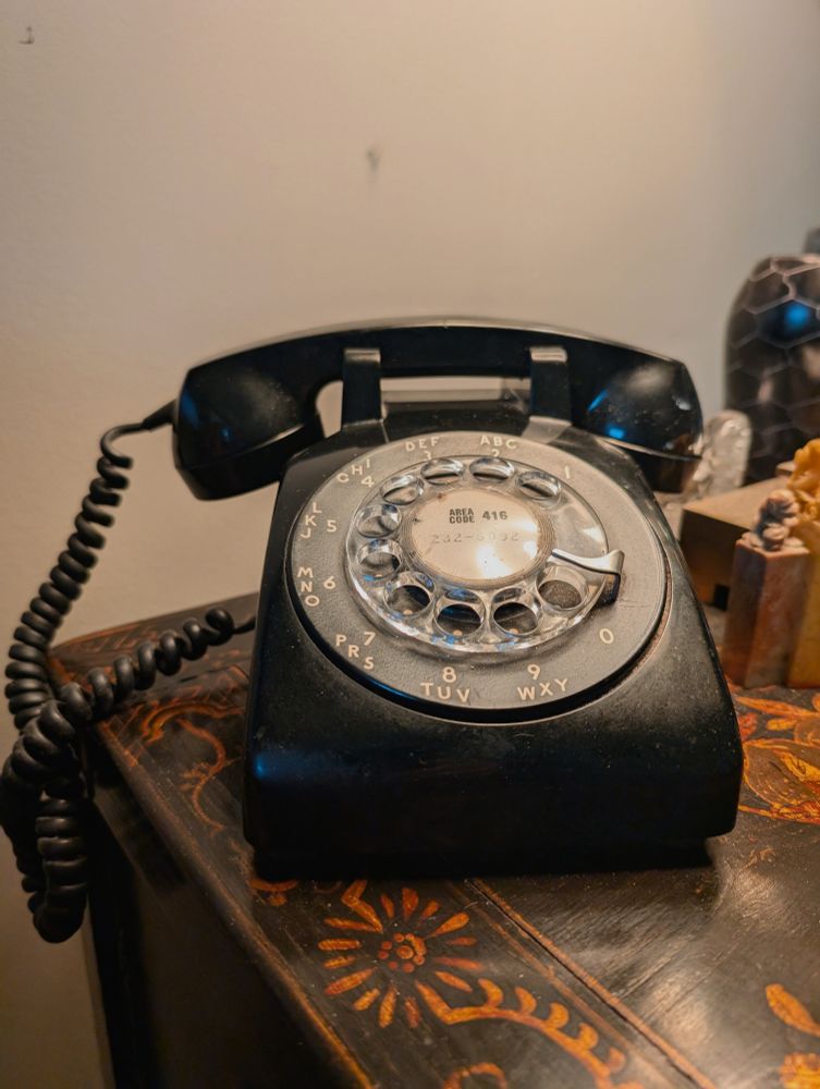 A plugged in functioning rotary phone on a side table.