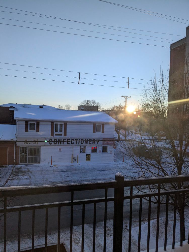The sun is on the horizon rising to greet a cool blue hued scene. The photo is taken from a balcony looking out to an old, but still functioning, confectionery across the street.