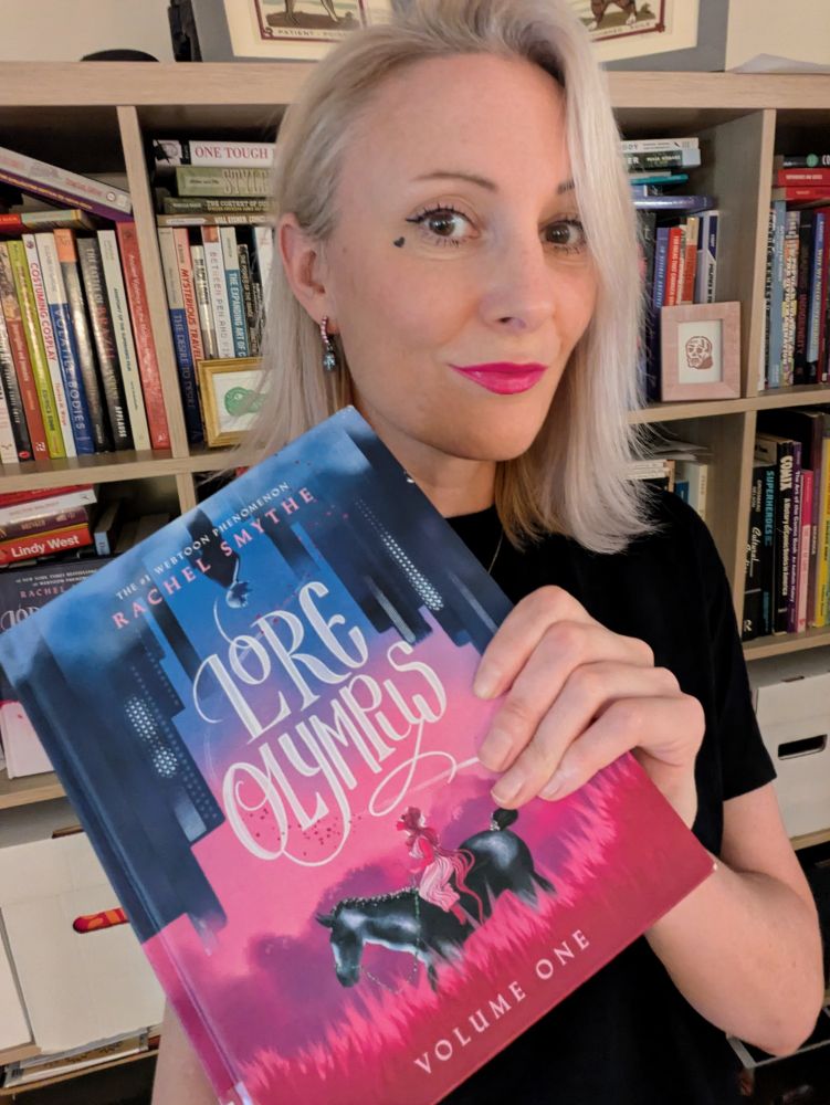 Me holding volume 1 of Rachel Smythe's Lore Olympus 