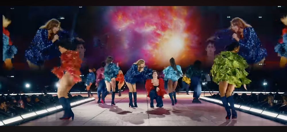 Taylor Swift and her dancers performing Karma at the eras tour. The background shows a star bursting in THE COLORS