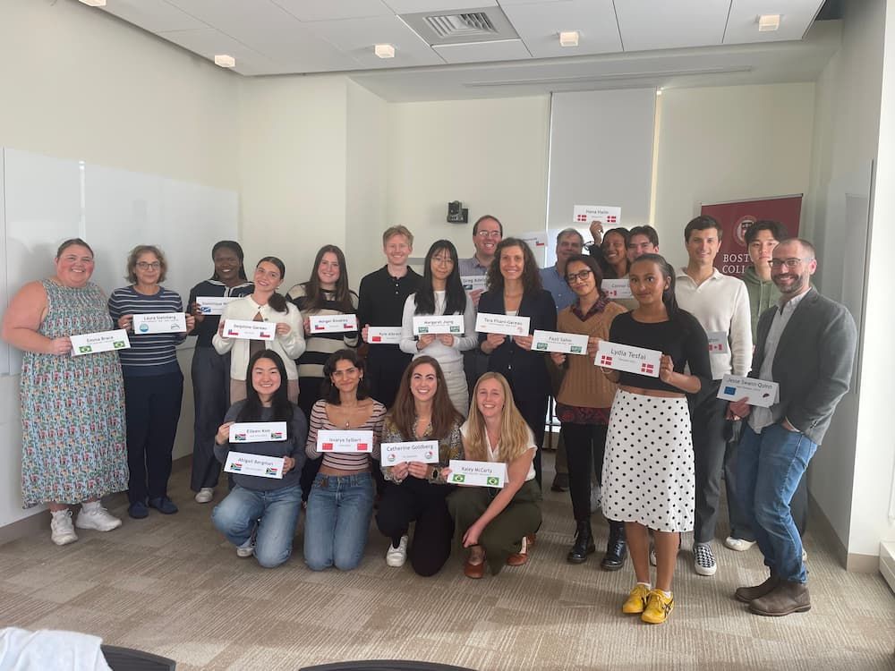 Group of Boston College students and faculty holding place cards in a classroom, smiling at the camera.