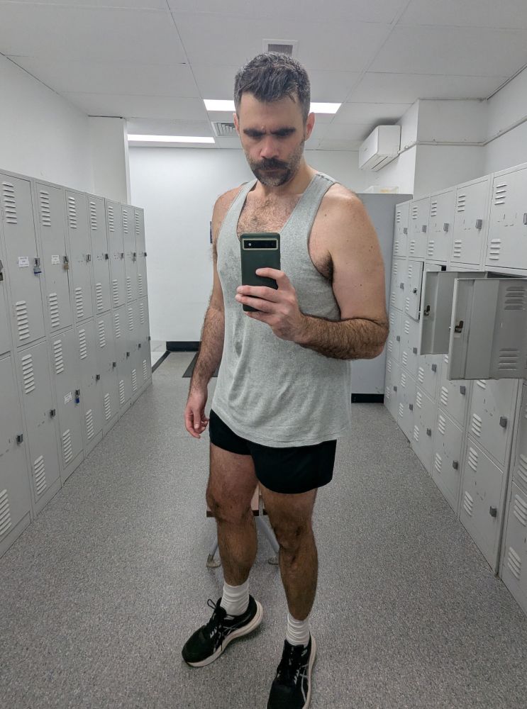 Gym selfie in mirror. Wearing grey singlet and black shorts. 