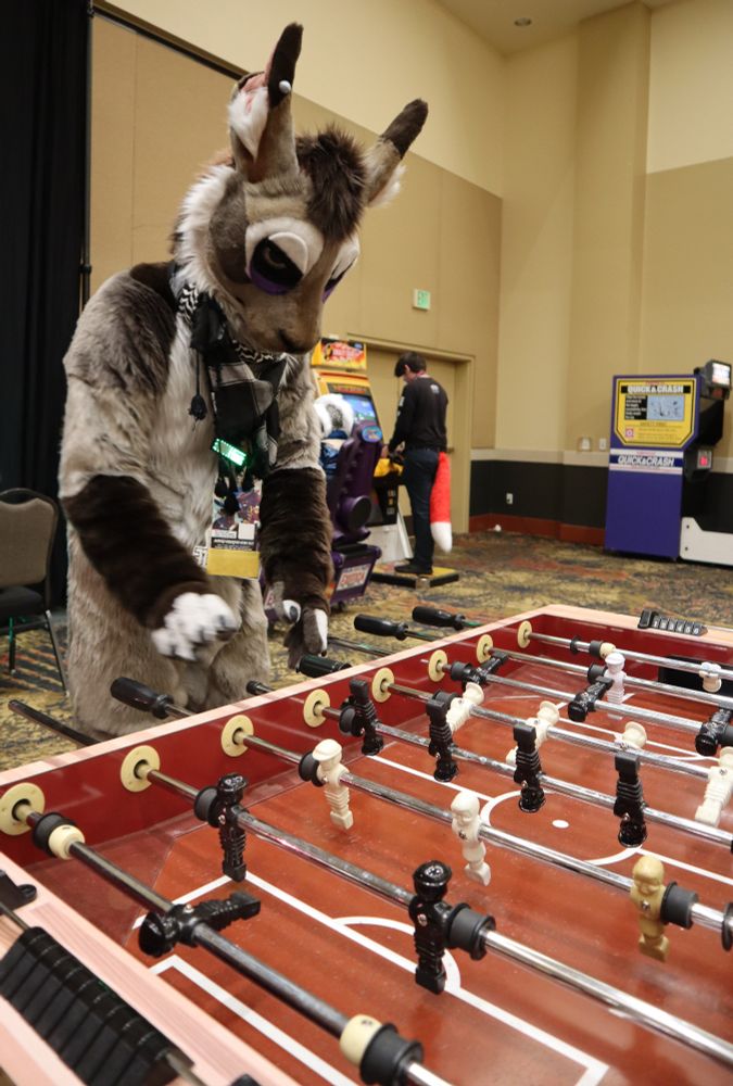 A hare fursuiter looking disgruntled playing foosball. 