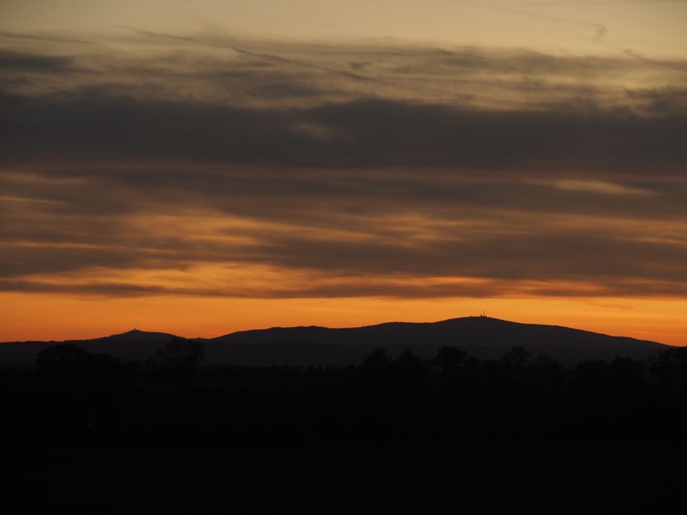 Die Silhouette des Brockens zeichnet sich schwarz vor orangenem Abendhimmel ab 