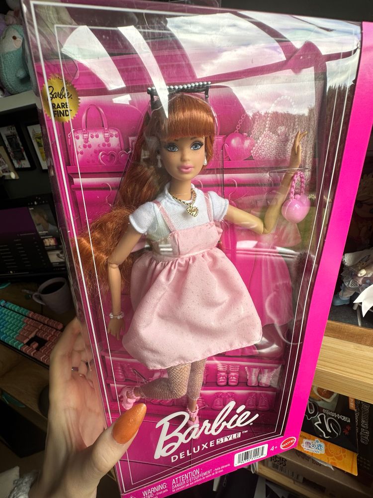 Barbie Deluxe Syle 2024 Edition. The rare Midge version. She has the Steffi face mold and the same outfit like the Milly Barbie: Pastel pink short dress with tiny dots and a white shirt underneath. A gold necklace, pink shoes, white fishnet socks and a tiny pink purse. Her hair is red