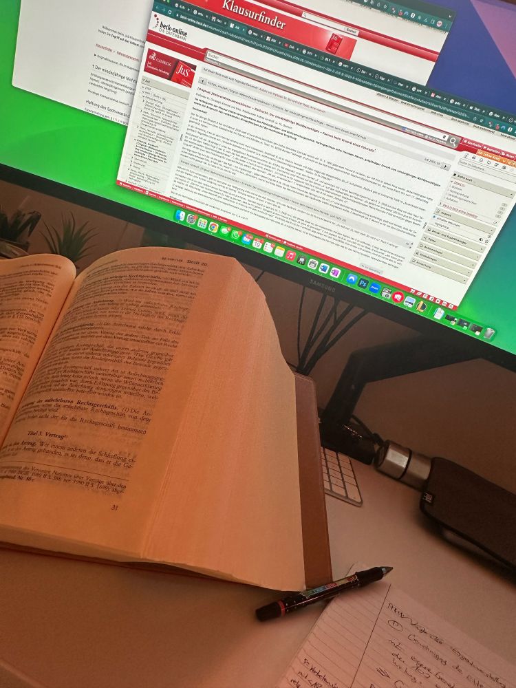 Geöffnetes Gesetzesbuch „Habersack“ steht vor Monitor, auf welchem ein Sachverhalt einer Übungsklausur geöffnet ist