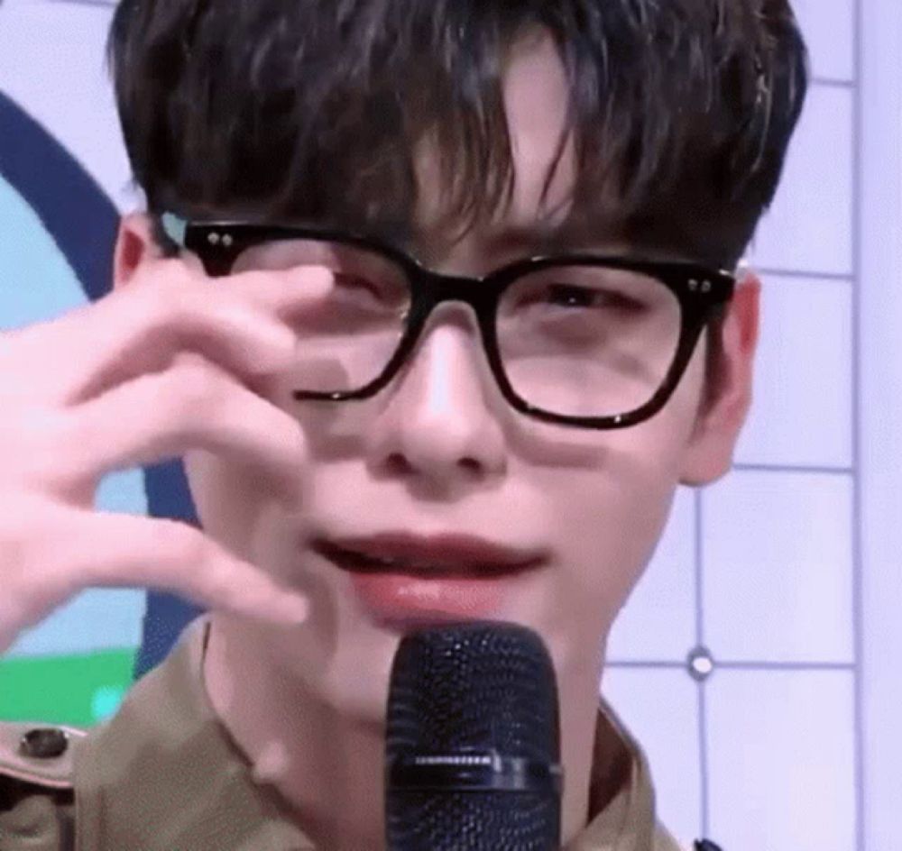 a young man wearing glasses is covering his eyes with his hand while speaking into a microphone .