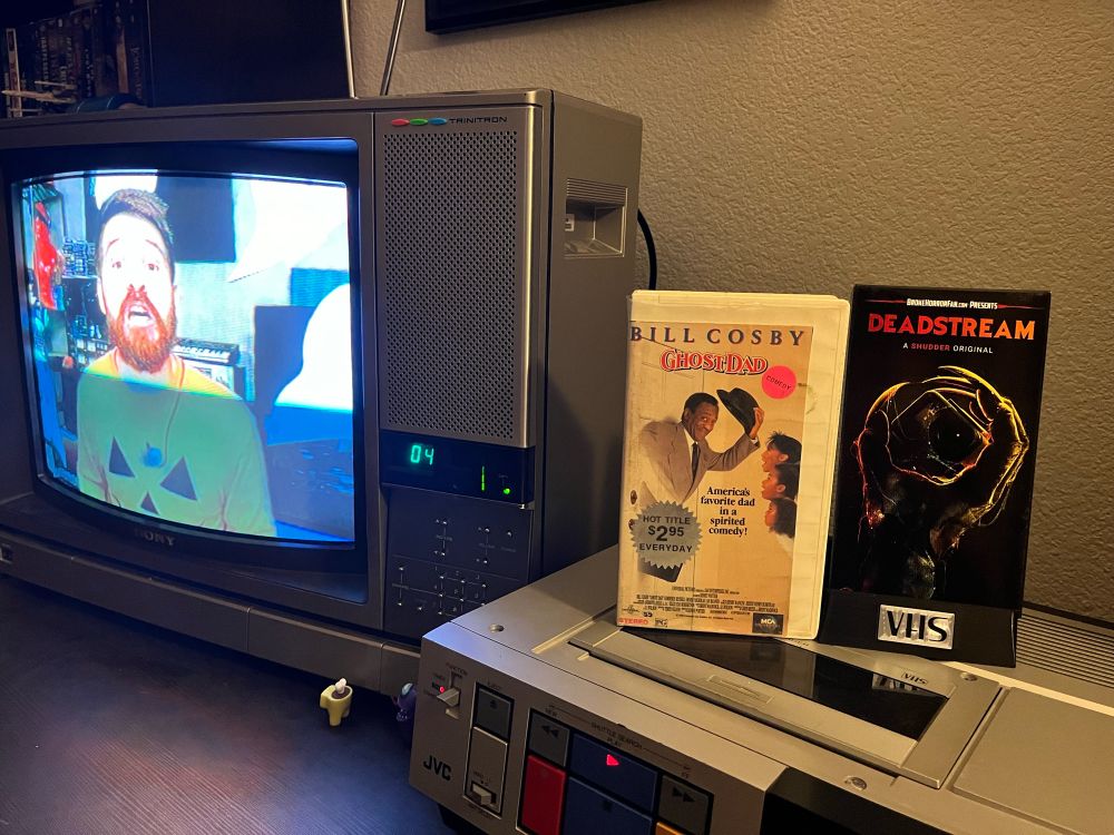 VCR and CRT tv playing Deadstream (2022) with the box on top of the VCR, and the case for Ghost Dad also on VHS 