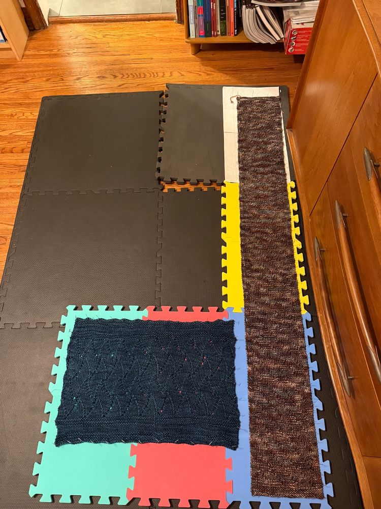 a blue cowl and brown scarf being wet blocked on foam tiles